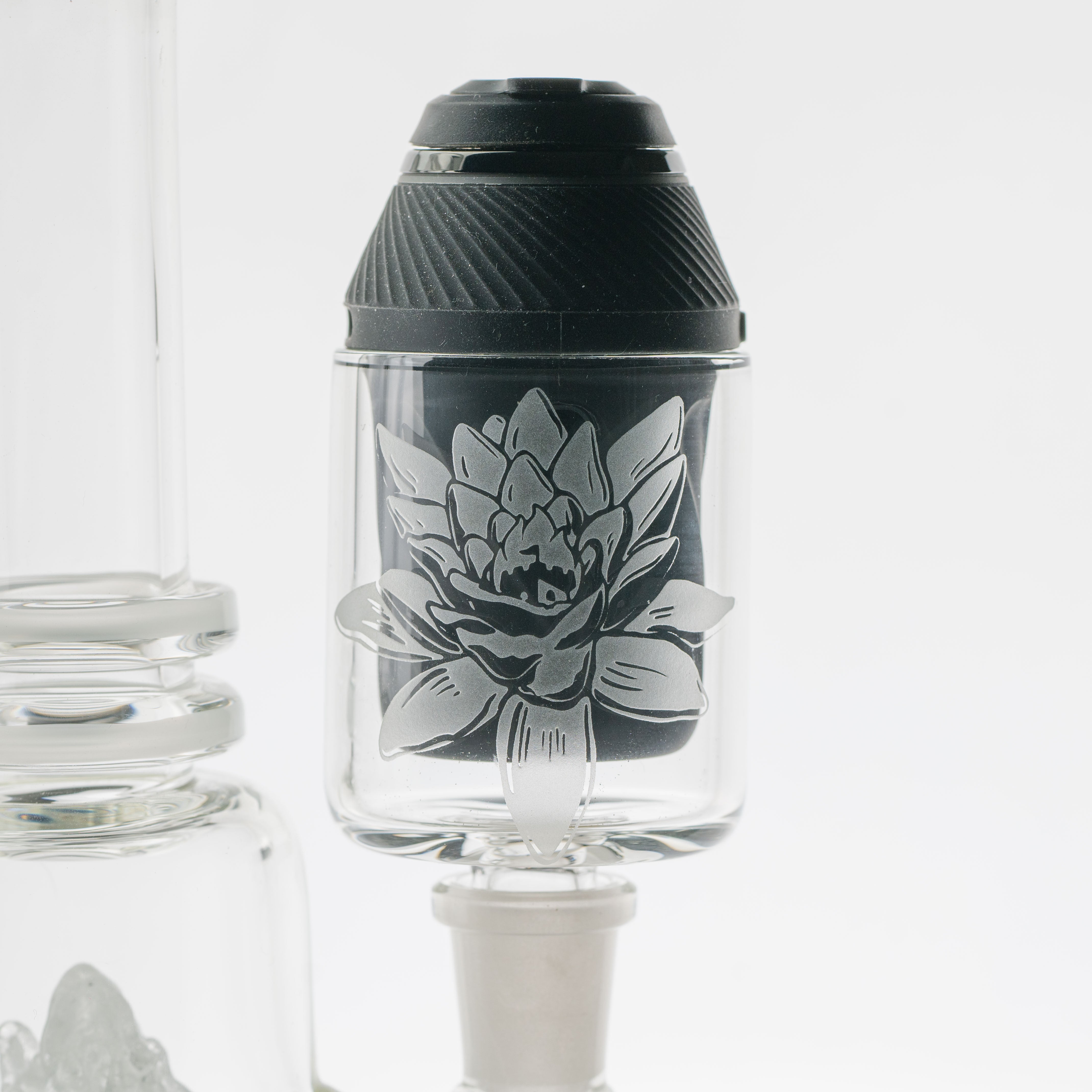 A front view of the PuffCo Proxy Glass Attachment, a frosted lotus-shaped piece positioned next to a clear glass container. A front view of the PuffCo Proxy Glass Attachment, a frosted lotus-shaped piece positioned next to a clear glass container.