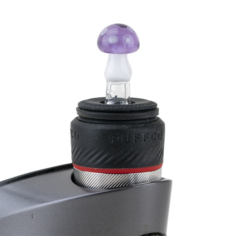 A close-up shows the Sriusly Shrooms PuffCo Peak Pro Glass Ball Cap, featuring a purple, mushroom-shaped glass dome. A close-up shows the Sriusly Shrooms PuffCo Peak Pro Glass Ball Cap, featuring a purple, mushroom-shaped glass dome.