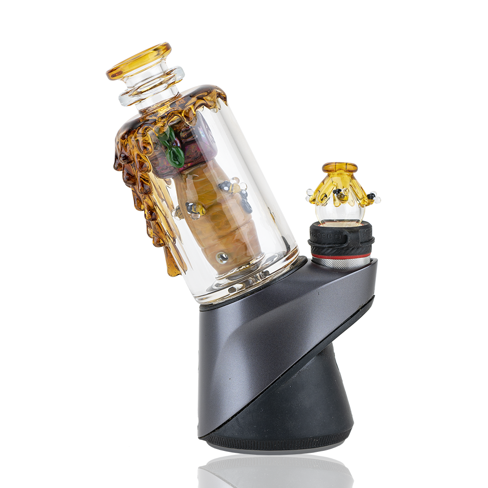A three-quarter view of the Save the Bees PuffCo Peak & Peak Pro Glass Attachment, displaying a patterned amber and clear glass design. A three-quarter view of the Save the Bees PuffCo Peak & Peak Pro Glass Attachment, displaying a patterned amber and clear glass design.