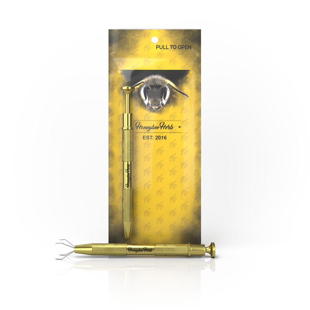 A close-up view of the Honeybee Dab Claw, a gold-toned tool with a textured grip, presented against a dark background. A close-up view of the Honeybee Dab Claw, a gold-toned tool with a textured grip, presented against a dark background.