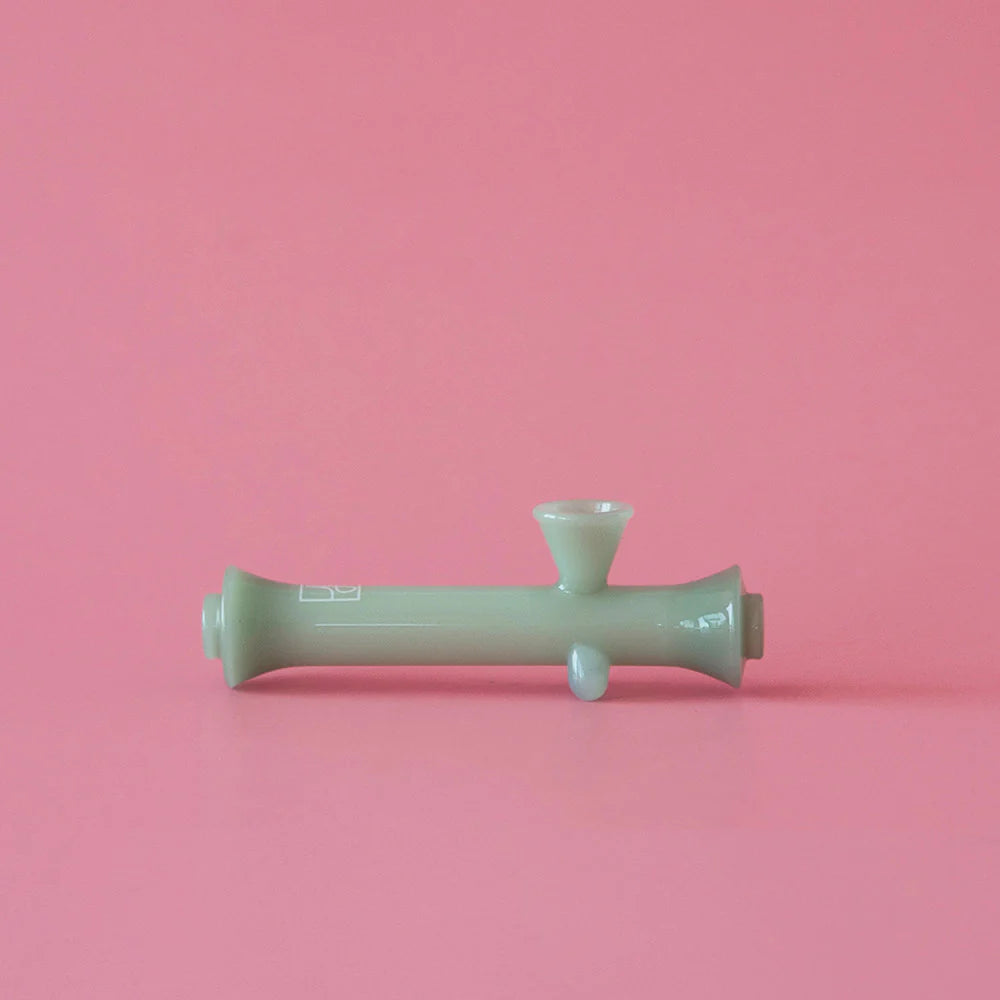 Front view of The Steamroller, a green glass pipe angled against a solid pink background. Front view of The Steamroller, a green glass pipe angled against a solid pink background.