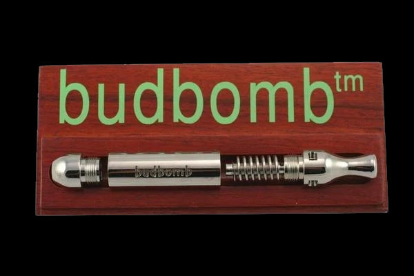 Front view of The Original Budbomb, a silver-colored pipe with etched detailing, set against a dark wood surface. Front view of The Original Budbomb, a silver-colored pipe with etched detailing, set against a dark wood surface.