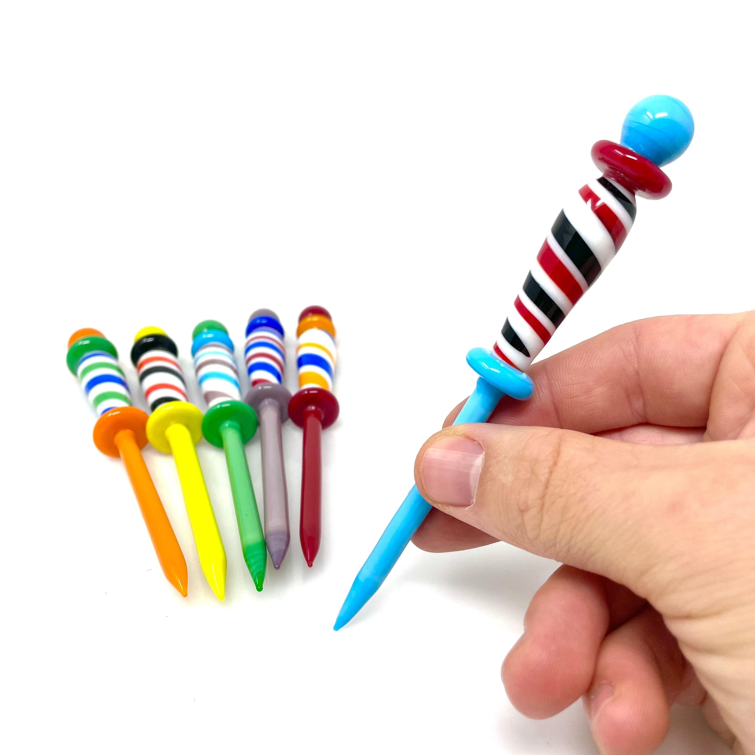 A hand holds a colorful Barber Dabber alongside several similar dabbing tools on a white background. A hand holds a colorful Barber Dabber alongside several similar dabbing tools on a white background.