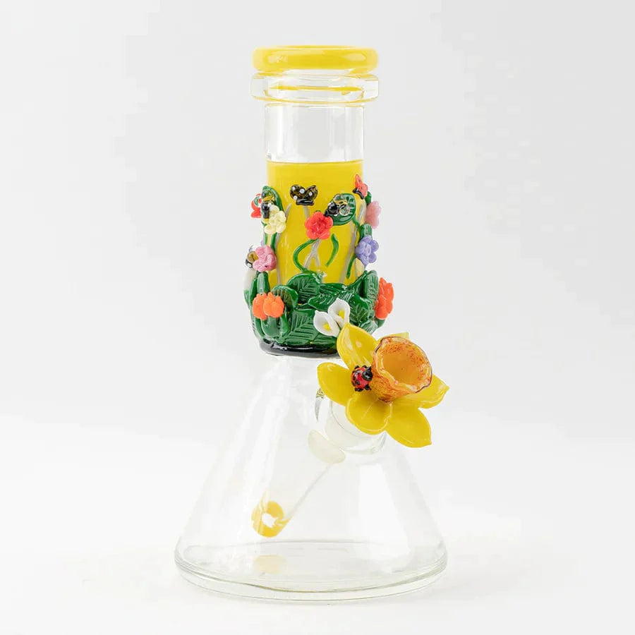 Front view of the Sunshine Garden Beaker Bong, showcasing a clear glass base with colorful floral embellishments around the neck. Front view of the Sunshine Garden Beaker Bong, showcasing a clear glass base with colorful floral embellishments around the neck.