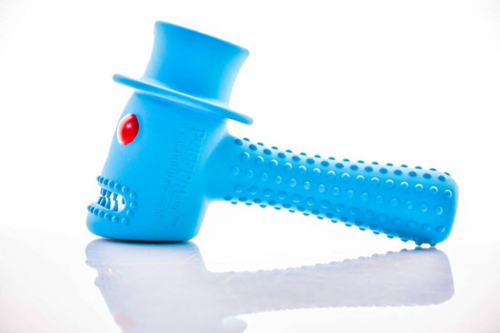 A brightly lit, angled view of the Hippie Hammer Dog Toy, reflecting on a glossy white surface. A brightly lit, angled view of the Hippie Hammer Dog Toy, reflecting on a glossy white surface.