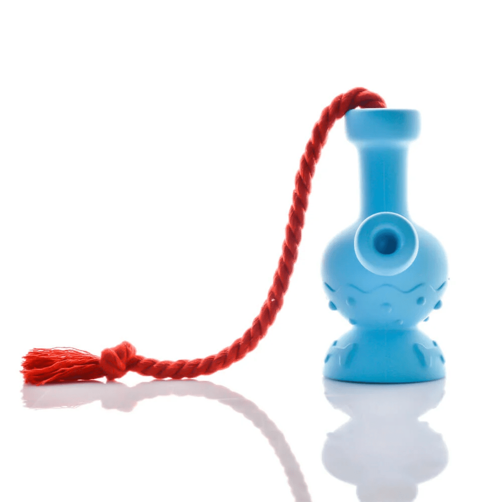 Front view of the Tug & Toke Dog Toy, a bright blue object with a red string, reflecting on a glossy surface. Front view of the Tug & Toke Dog Toy, a bright blue object with a red string, reflecting on a glossy surface.