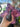 A hand holds the small, dark gray Baby Elephant Sherlock Pipe, its curved form highlighted against a blurred purple background.