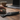 Close-up of the black XVAPE LANZA vape laid open on a wooden table with a hand holding a metal grinder and a blurred laptop and coffee cup in the background