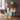 Close-up, three-quarter view of the Cheech and Chong Up in Smoke Pedro 8" Bong with a white neck and green accents, sitting on a wooden table beside a blue birthday cake with lit candles.