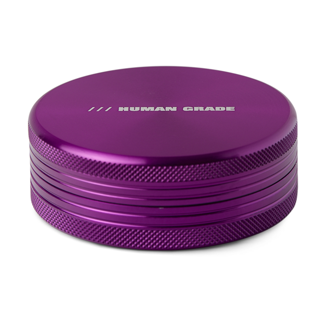 A close-up, angled view of the Grinder 1C with a metallic purple finish and textured circular layers.