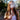 Woman holding the Cipher NOVA | Stainless Steel - V2 vaporizer vertically at chest height, exhaling a cloud of vapor with a sunlit backyard blurred behind her.