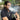 Three-quarter view of a person exhaling a thick cloud of vapor while holding the Cipher NOVA | Stainless Steel - V2 vape pen near a riverside with trees in soft daylight