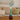 Close-up frontal view of the My Bud Vase "Mermaid" Ocean Goddess Bong showing its turquoise-green mermaid-tail neck, cream tail-fluke rim, and decorative blue sprig against a blurred sofa backdrop