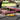 Close-up of a yellow Cloud 8 Silicone Pizza Slice Hand Pipe resting on a wooden picnic table in front of a red-check pizza box with melting cheese.