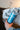 Close-up view of the Pure Isopropyl Alcohol bottle held in a hand, displaying the clear liquid inside against a blurred background.