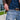 A close-up, angled view shows the Premium Storage Tube peeking out of a jeans pocket, alongside a brown leather belt.
